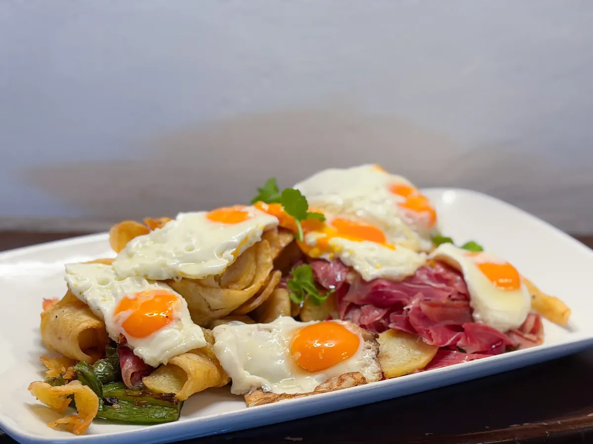 Huevos rotos con jamón, patatas y pimientos de Padrón, ración generosa de tapería en el barrio marinero de Bouzas