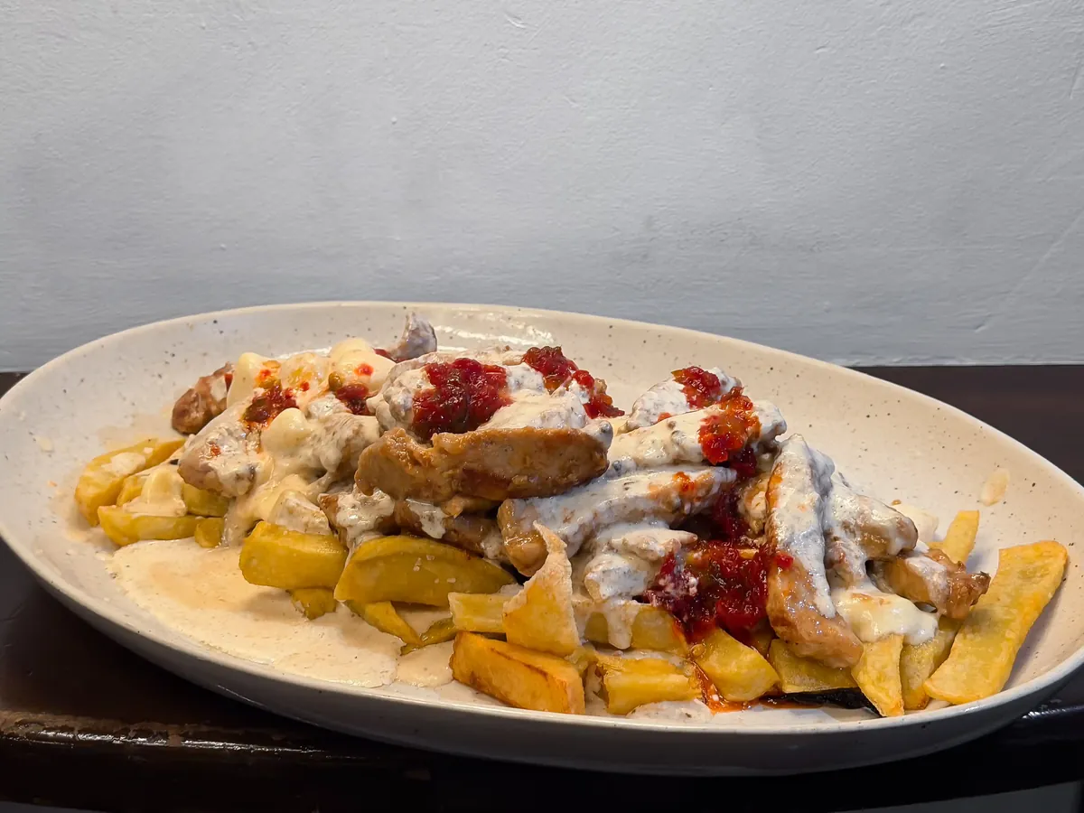 Raxo de cerdo con salsa cremosa de queso y patatas fritas, plato contundente de cocina tradicional en restaurante de Bouzas