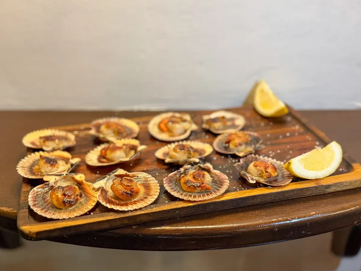 Volandeiras a la plancha con limón sobre tabla de madera, marisco típico gallego servido en Habemus Bouzas, Vigo